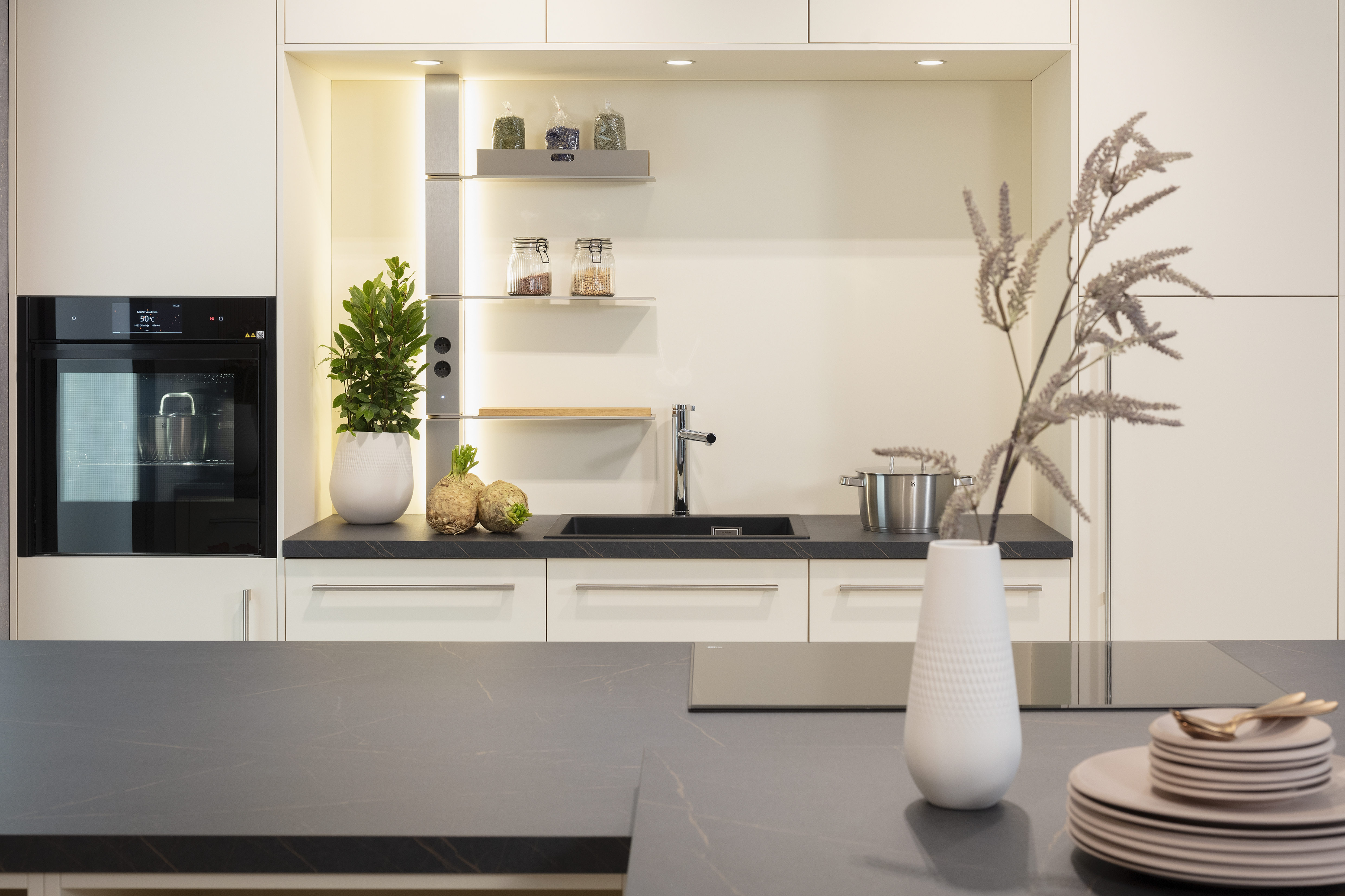 Nischenrückwand in Macaronmatt mit dunkler Arbeitsplatte im Vordergrund