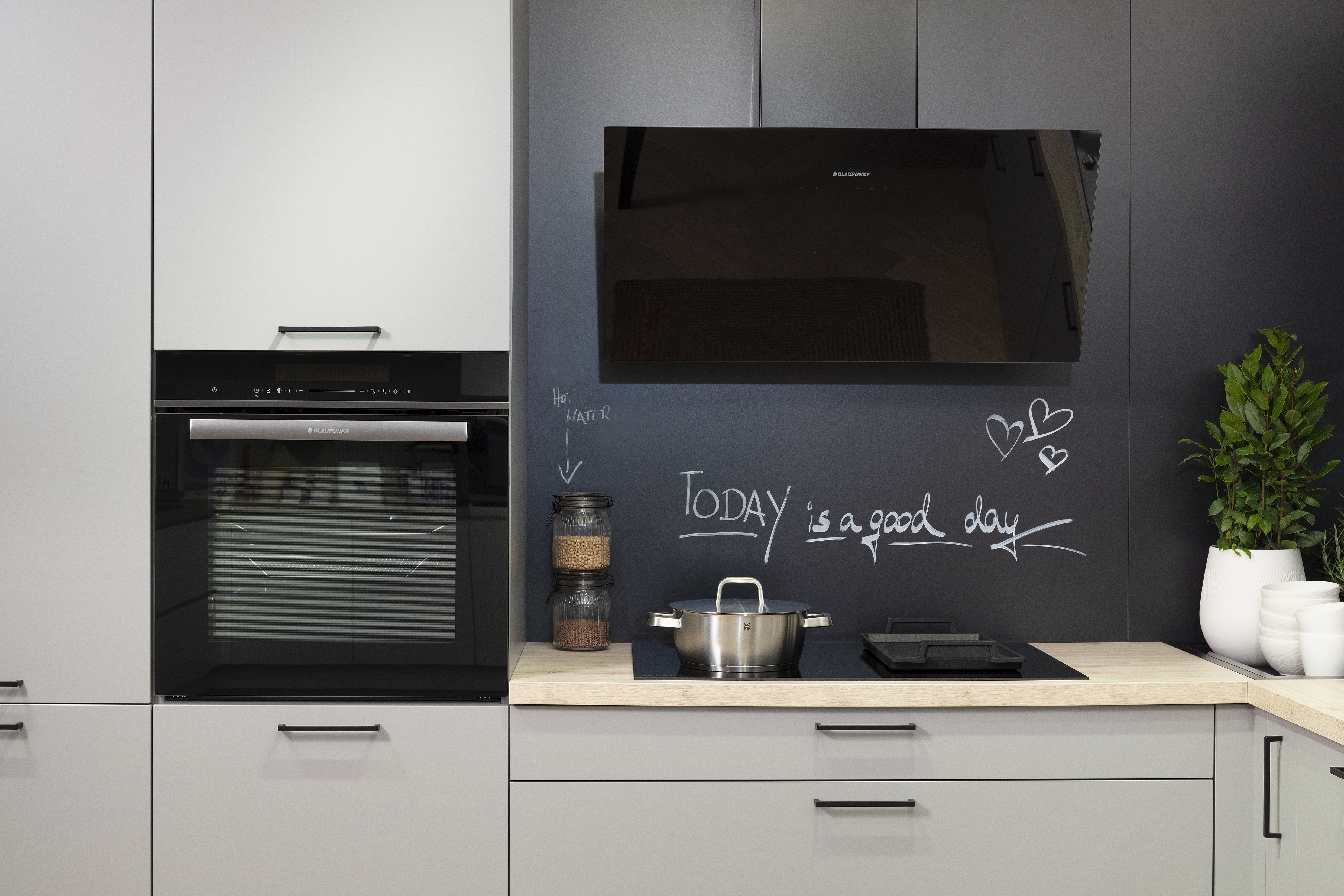 Häcker-Küche in Perlgrau Lacklaminat mit Kopffreihaube, Kochfeld und Backofen. 