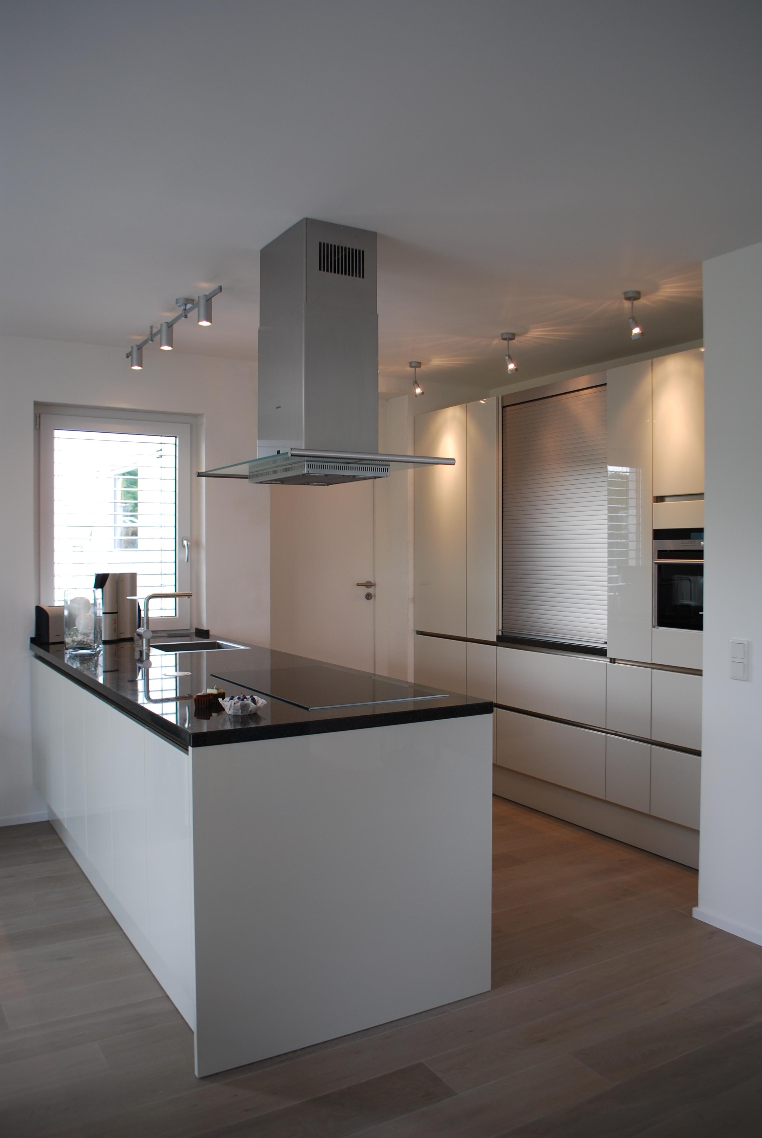 Kücheninsel mit glänzender Steinarbeitsplatte, im Hintergrund Hochschränke mit einem Jalousieschrank