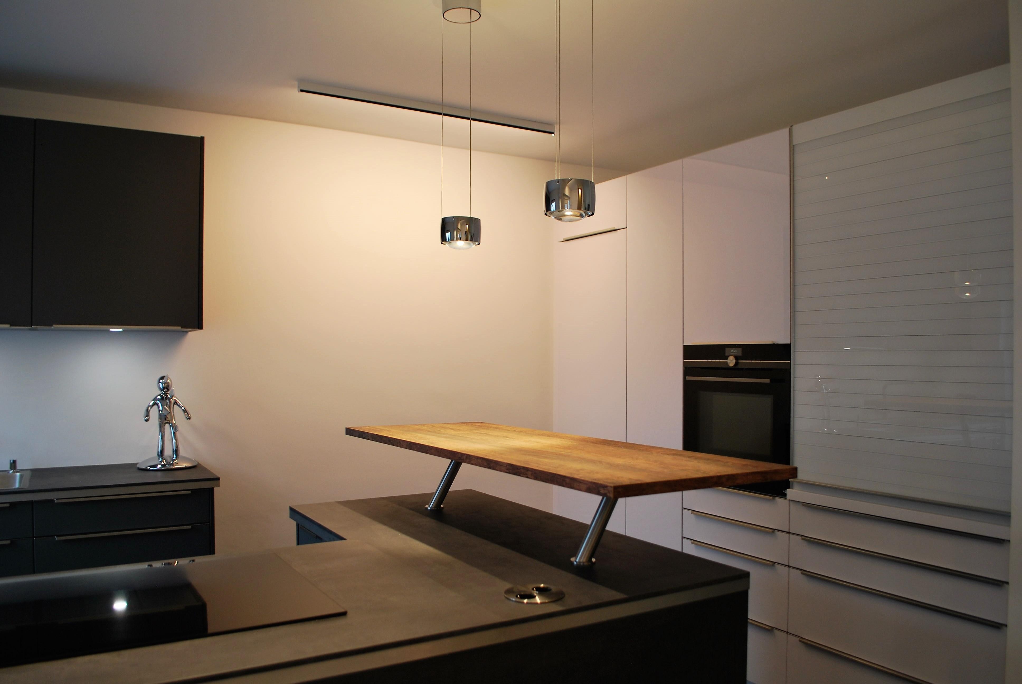 Hochgesetzter Holztresen auf einer Kücheninsel, im Hintergrund Hochschränke mit hochgebautem Backofen