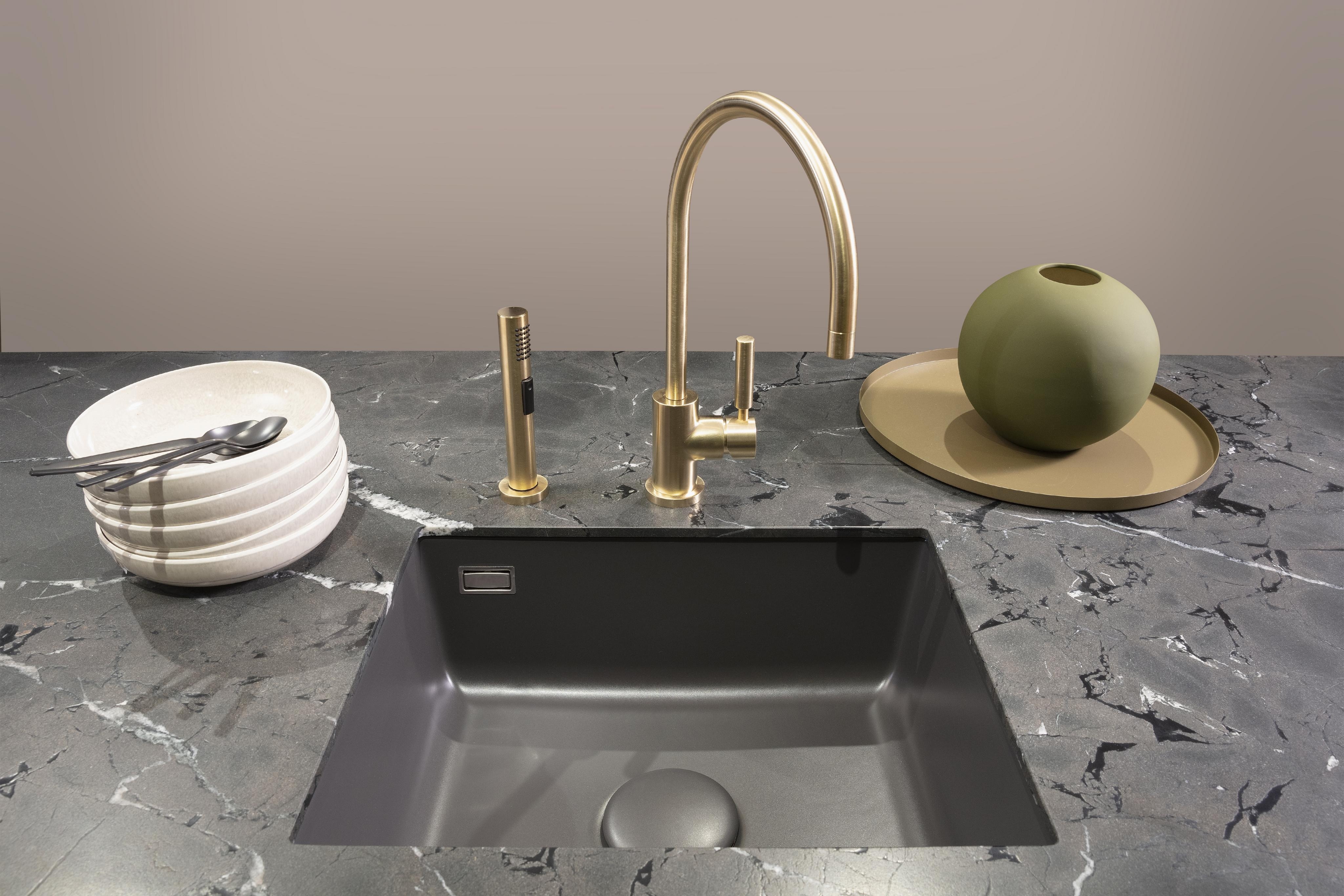 Untergebautes Spülbecken mit goldener Armatur in einer Steinarbeitsplatte