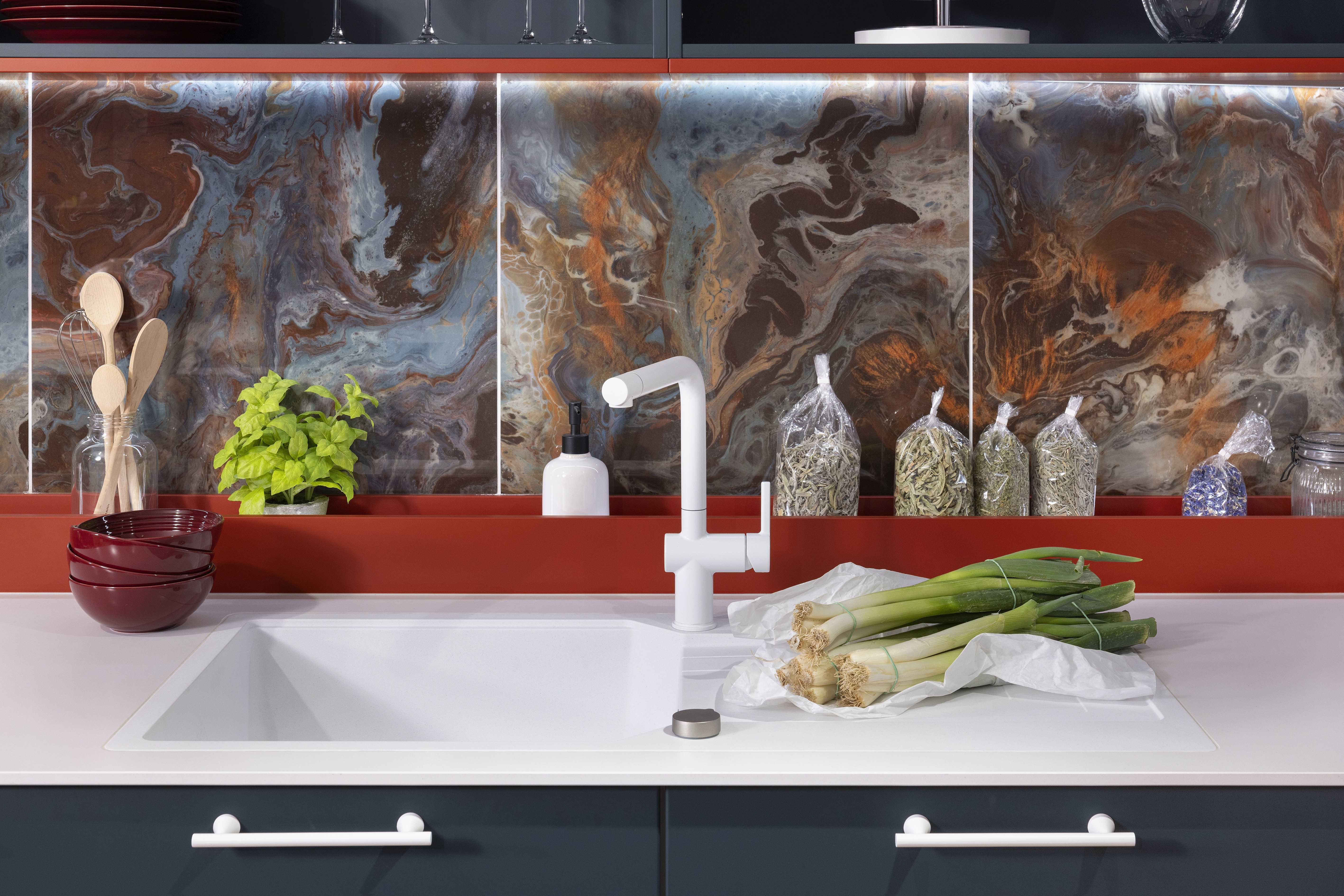 APL: Systeme Blanco Zeus matt Front: Herbstrot samtmatt AFP Front: Tiefblau samtmatt AFP Korpus: Kristallweiß/Naturweiß Griff: Metall Weiß lackiert Geräte: Siemens, Abzugshaube Airforce Armatur: Franke Spüle: Franke   Features: Farbe in der Küche, quadratische Kücheninsel mit Kochfeld und Dunstabzug, Kontrastelemente in Weiß (Griffe, APL, Spüle, Wasserhahn und Backofen), weißer BACKOFEN, kleine Designküche, junge Küche, Nischenrückwand als Motivfliese (Schüller), Arbeitsplatz, „versteckte“ Kaffeeküche 