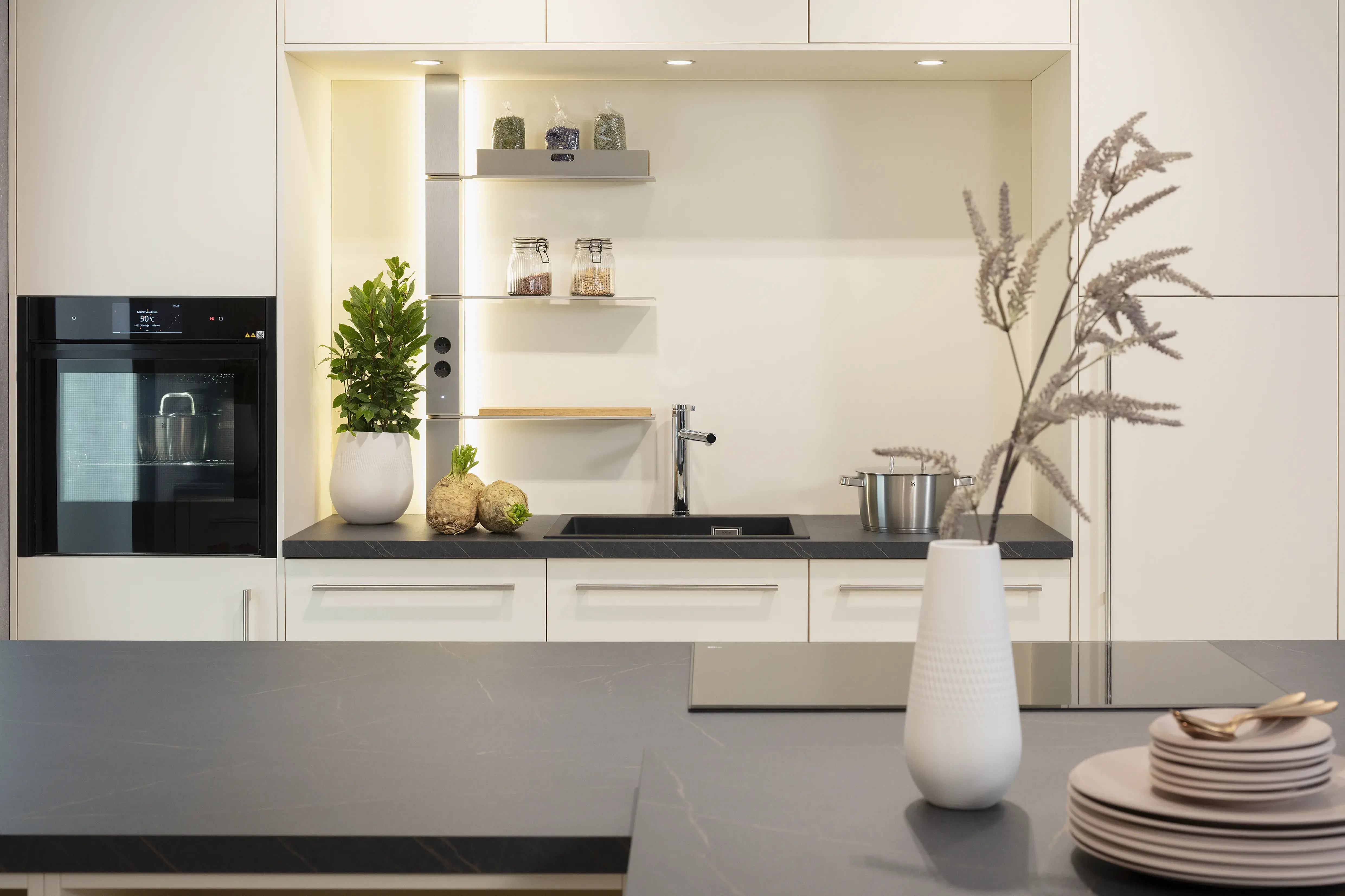 Nischenrückwand in Macaronmatt mit dunkler Arbeitsplatte im Vordergrund