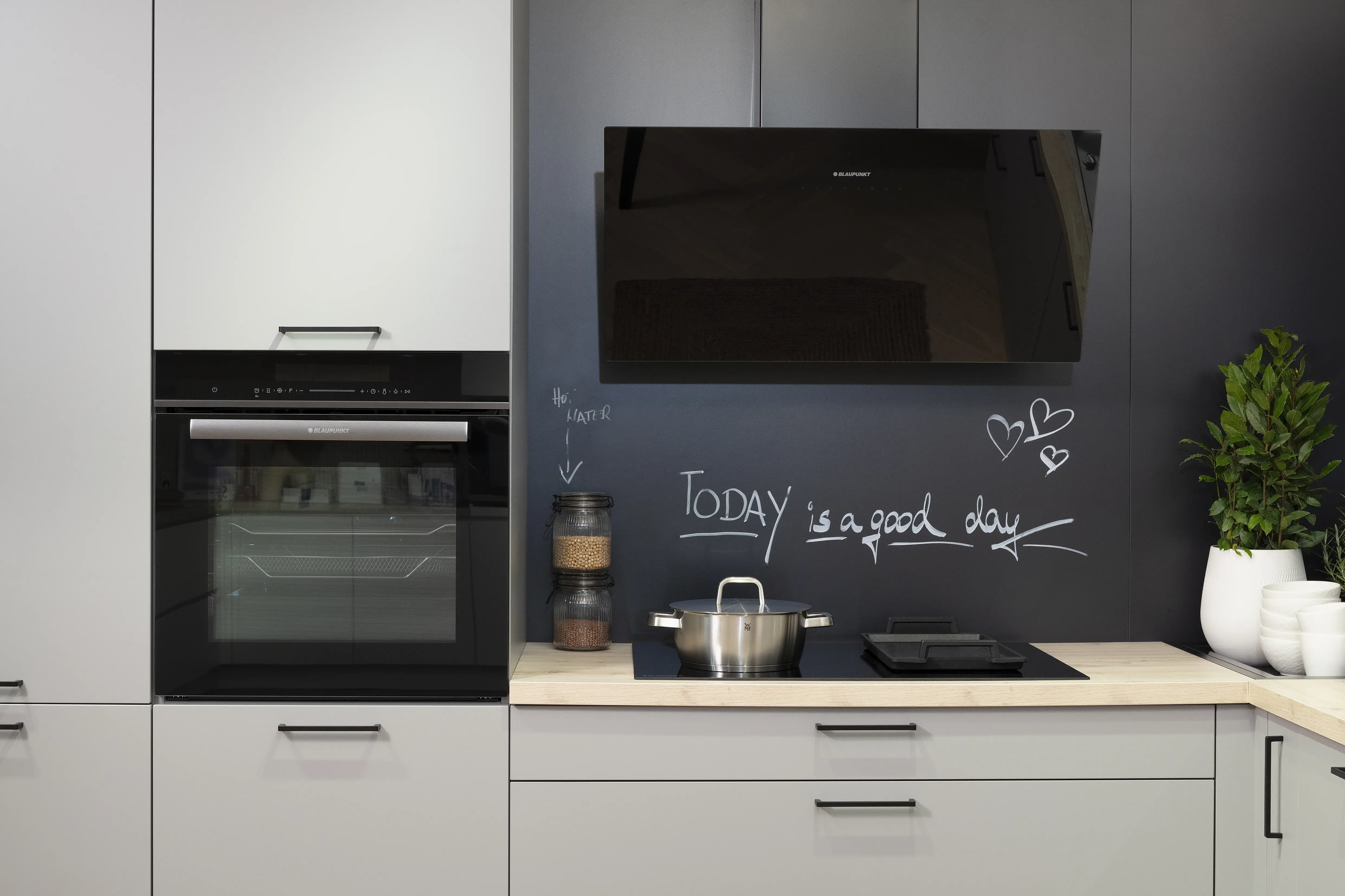 Häcker-Küche in Perlgrau Lacklaminat mit Kopffreihaube, Kochfeld und Backofen. 