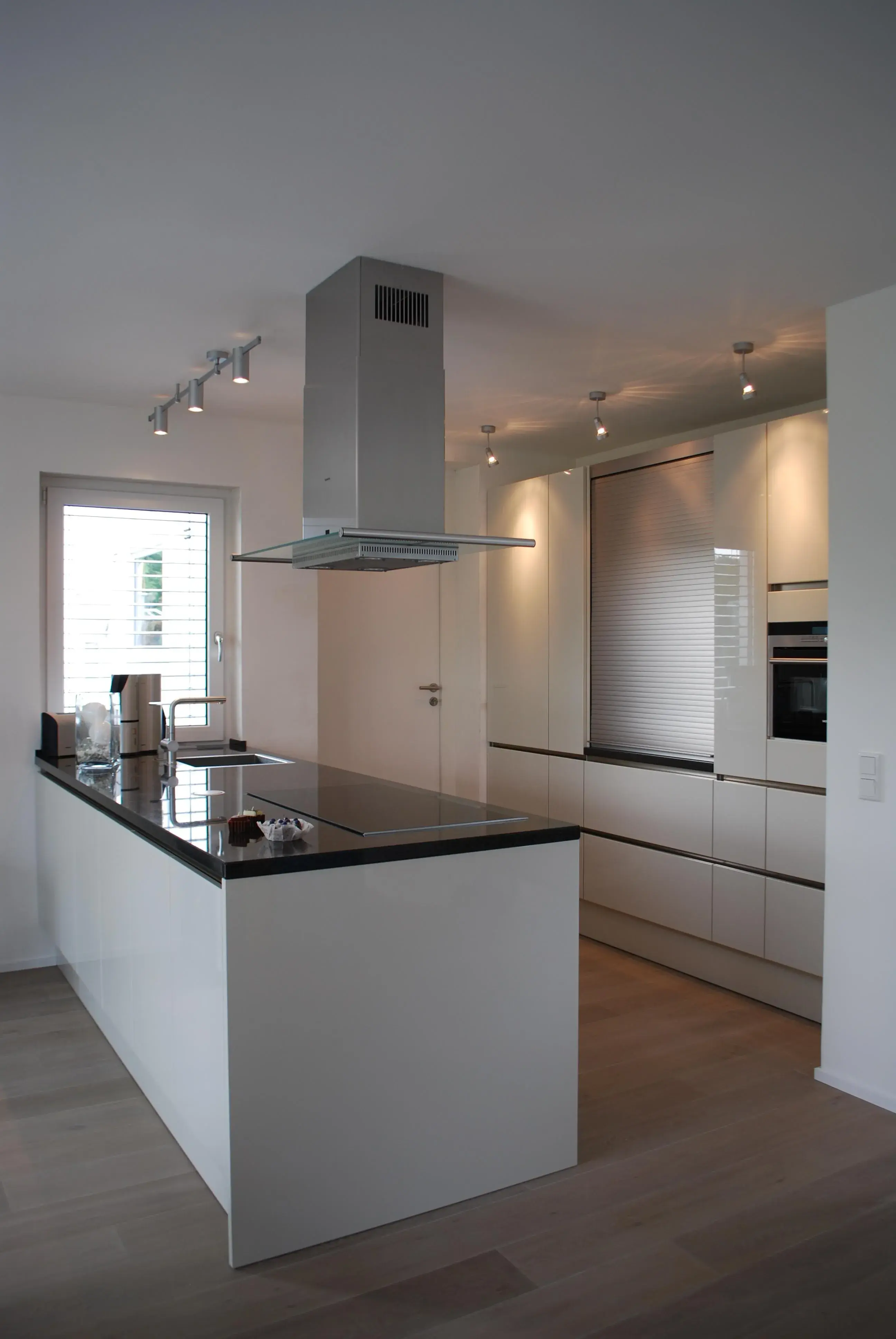 Kücheninsel mit glänzender Steinarbeitsplatte, im Hintergrund Hochschränke mit einem Jalousieschrank